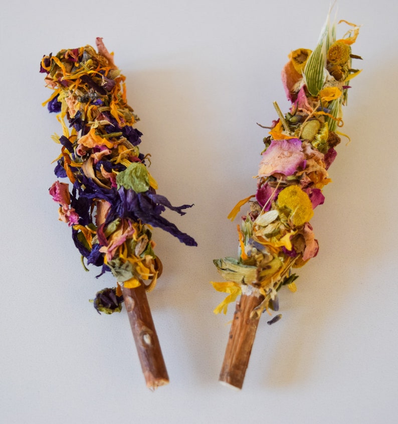 K&ouml;nnte beinhalten: Zwei R&auml;ucherb&uuml;ndel aus getrockneten Blumen. Die St&auml;be sind mit einer Vielzahl von bunten getrockneten Blumen umwickelt, darunter lila, orange, gelbe und rosa Bl&uuml;tenbl&auml;tter. Die St&auml;be haben einen nat&uuml;rlichen Holzgriff.