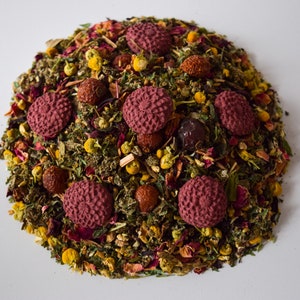 Pu&ograve; includere: Un primo piano di un blend di t&egrave; sfuso con una variet&agrave; di erbe, fiori e bacche essiccate. Il blend di t&egrave; &egrave; disposto in forma circolare con accenti rossi, rosa e gialli.