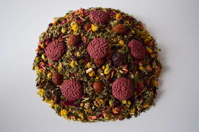 Pu&ograve; includere: Un primo piano di un blend di t&egrave; sfuso con una variet&agrave; di erbe, fiori e bacche essiccate. Il blend di t&egrave; &egrave; disposto in forma circolare con accenti rossi, rosa e gialli.