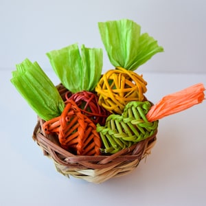 May include: A woven wicker basket filled with colorful, handmade carrot-shaped toys. The toys are made of woven paper and come in shades of green, orange, and yellow.