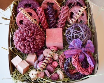 Può includere: Una scatola regalo rosa e viola piena di oggetti naturali e tessuti, tra cui una pigna rosa e viola, una palla intrecciata rosa e viola e un anello intrecciato rosa e viola.