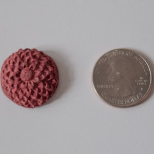 Pu&ograve; includere: Un primo piano di un piccolo bottone a forma di fiore rosso lavorato a uncinetto. Il bottone &egrave; circa delle dimensioni di una moneta da 25 centesimi di dollaro americano.