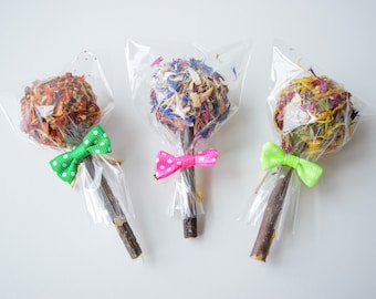 Può includere: Tre piccoli mazzi di fiori secchi avvolti in plastica trasparente con un bastoncino di legno e un fiocco. I mazzi sono legati con fiocchi verdi, rosa e verdi con pois bianchi.