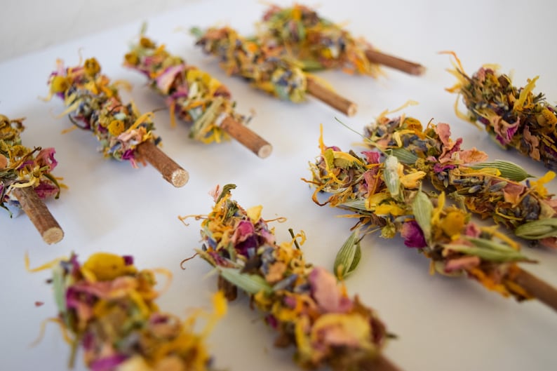 K&ouml;nnte beinhalten: Nahaufnahme von mehreren Trockenblumen-B&uuml;ndeln auf Holzst&auml;ben. Die B&uuml;ndel bestehen aus bunten getrockneten Bl&uuml;tenbl&auml;ttern, Bl&auml;ttern und Knospen in Gelb-, Rosa-, Lila- und Gr&uuml;nt&ouml;nen. Die St&auml;be sind naturbraun.
