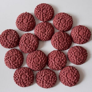 Pu&ograve; includere: Una collezione di 15 bottoni decorativi rotondi di colore bordeaux con un design floreale in rilievo. I bottoni sono disposti in cerchio su uno sfondo bianco.