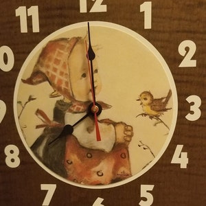 May include: A brown wooden clock with a white face and black hands. The clock face features a painting of a little girl in a red and white dress looking at a yellow bird. The numbers on the clock are white and the clock says "Quarz" at the bottom.