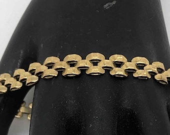 May include: A gold-toned bracelet with a chain link design. The links are square-shaped and have a textured surface.