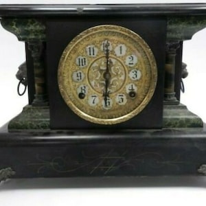 May include: Antique black and green mantle clock with a gold face and Roman numeral hour markers. The clock has a decorative design on the base and lion head finials.