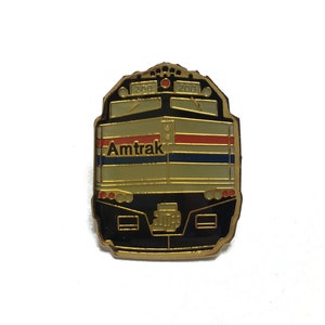 May include: Gold-colored Amtrak train engine pin with the Amtrak logo and the numbers 200 and 200 on the top.