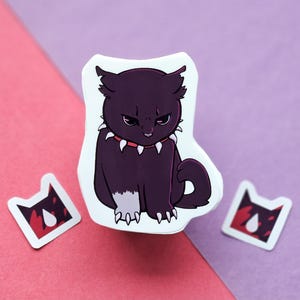 May include: A sticker featuring a dark purple cat with an angry expression, wearing a red collar with white spikes. Two smaller stickers with a cat head design and a red and white pattern are also present.