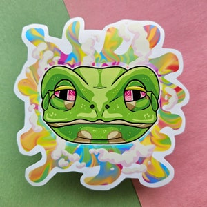 May include: A green frog sticker with red-rimmed eyes and a relaxed expression. The frog is surrounded by a colorful, swirling design with a vapor-like effect. The sticker has a white border and is set against a pink and green background.