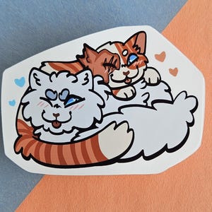 May include: A sticker featuring two cartoon cats cuddling. One cat is white with orange stripes, the other is orange and white. Both cats have blue eyes and are surrounded by small hearts.