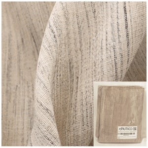 Peut inclure: Gros plan sur un tissu en lin beige avec un tissage texturé. Le tissu est drapé, montrant des plis et des ombres. Une petite image dans le coin montre le tissu plié et emballé, avec la marque HAUTICO visible.