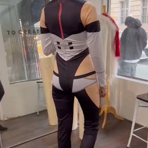 May include: A person wearing a black and white jumpsuit with a red stripe down the back. The jumpsuit has a white panel on the back with a geometric design. The person is standing in a store with a mirror behind them.