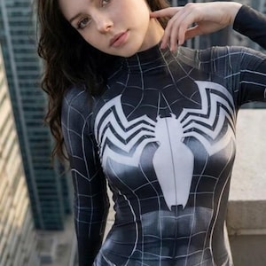 May include: A long-sleeved bodysuit featuring a black and white spider web pattern with a large white spider emblem centered on the chest. The garment has a high mock neck collar and a form-fitting design with shaded details to create a textured look.