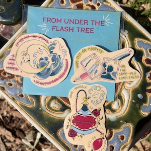 Puede incluir: Tres pegatinas ilustradas con una luna y olas azules, blancas y amarillas, un sello rojo, blanco y azul con un lápiz y una botella azul con rosas rojas y el texto "perfume barato". Las pegatinas tienen un fondo marrón claro y están sobre un fondo azul con el texto "FROM UNDER THE FLASH TREE".