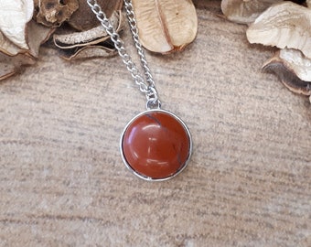 Op de afbeelding: Een zilveren ketting met een ronde, rode edelsteen hanger. De hanger is gezet in een zilveren bezel.
