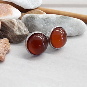 Może przedstawiać: Para srebrnych kolczyków z okrągłymi, pomarańczowo-brązowymi kamieniami.