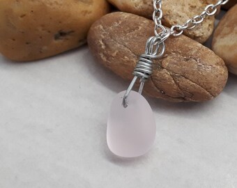 Pode incluir: Um delicado colar de corrente de prata com um pingente de vidro do mar rosa pálido envolto em fio de prata.