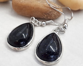 May include: A pair of silver teardrop earrings with dark blue gemstone accents.