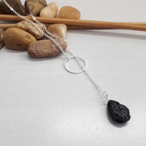 Puede incluir: Un collar de cadena de plata con un pequeño colgante circular y un colgante de roca de lava negra.