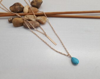May include: A layered gold necklace with a turquoise teardrop pendant and a thin gold bar pendant.