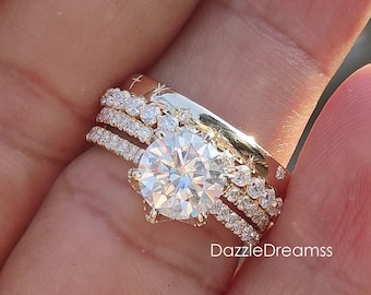 May include: A gold ring set with a large, round, clear gemstone surrounded by smaller gemstones. The ring is worn on a finger and is part of a three-piece set.