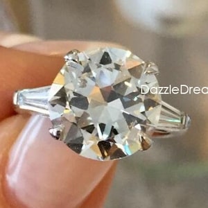 May include: A silver engagement ring with a large, round, clear diamond center stone and two smaller, baguette-shaped diamonds on either side.