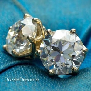 Puede incluir: Dos piedras preciosas redondas y facetadas, transparentes, engastadas en monturas de oro. Las piedras preciosas están sobre un fondo de tela azul.