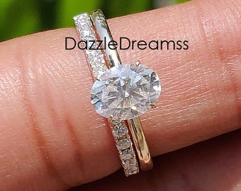 Pode incluir: Um conjunto de anéis de duas peças com uma banda dourada com pequenas pedras transparentes e uma banda dourada com uma pedra transparente grande em forma oval. O texto "DazzleDreamss" é visível.