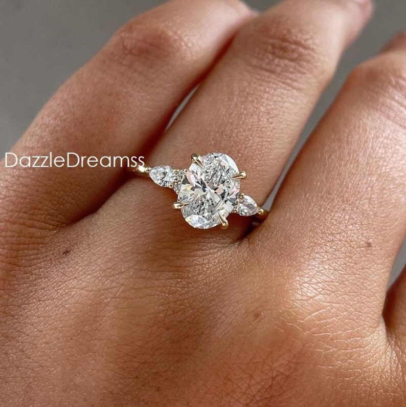 May include: A gold engagement ring with a large oval-shaped diamond and two smaller pear-shaped diamonds on either side.