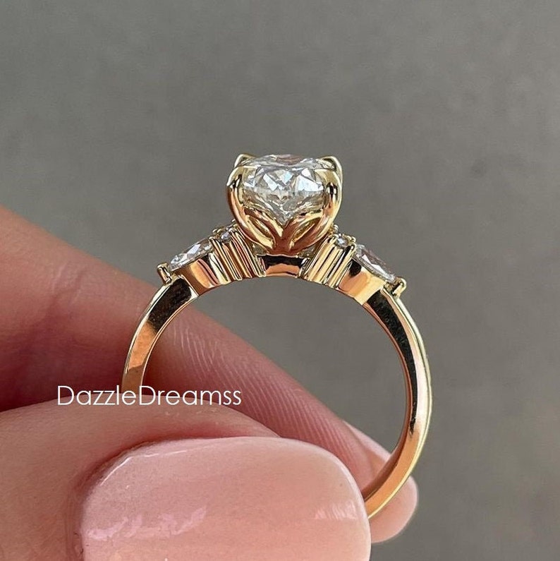 May include: A gold engagement ring with a large, round, clear center stone and two smaller, clear stones on either side. The ring has a delicate, floral design.