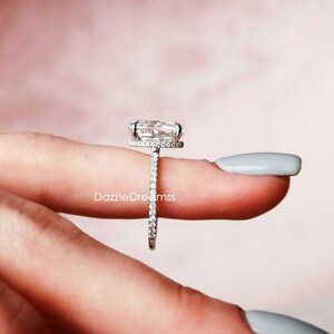May include: A silver engagement ring with a large oval-shaped center stone and a halo of smaller stones. The band is also set with smaller stones.