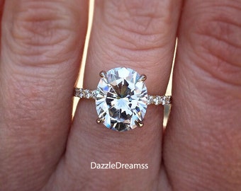 May include: Close-up of a gold ring with a large, oval-cut diamond center stone. The band is adorned with smaller, sparkling stones. The ring is set against a blurred background, highlighting the intricate details of the jewelry.