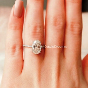 May include: A silver ring with a large oval-shaped diamond set in a pave setting. The ring is on a person's finger.