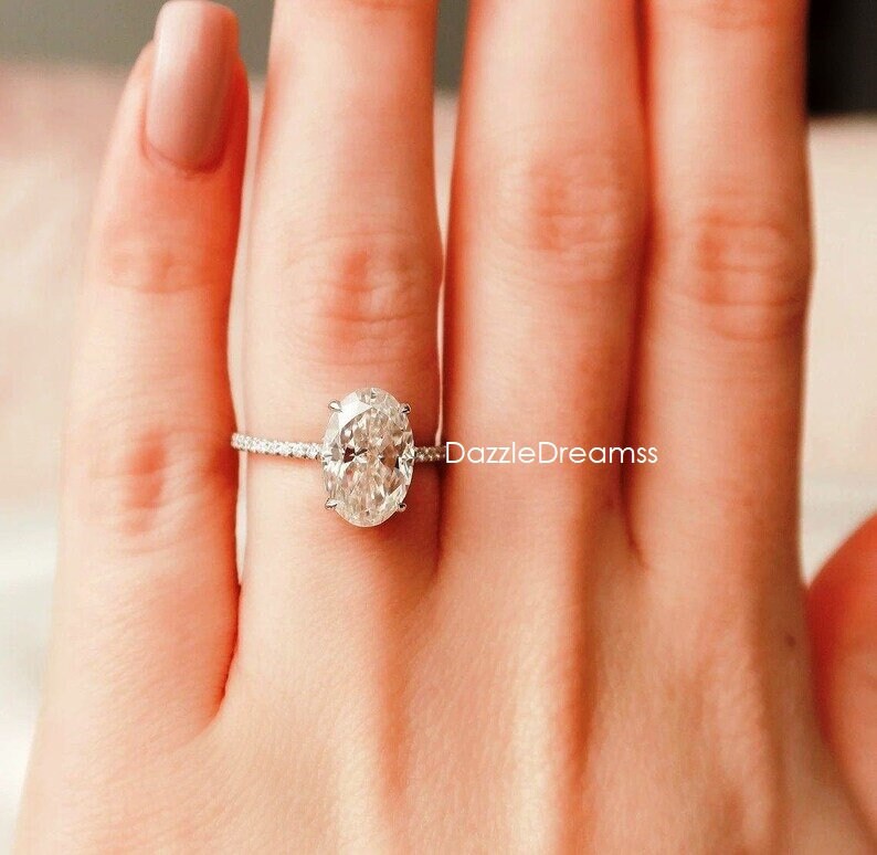 May include: A silver ring with a large oval-shaped diamond set in a pave setting. The ring is on a person's finger.