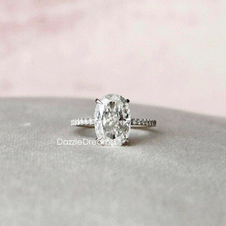 May include: A silver engagement ring with a large oval-shaped diamond. The ring has a thin band with small diamonds set in a pave setting.