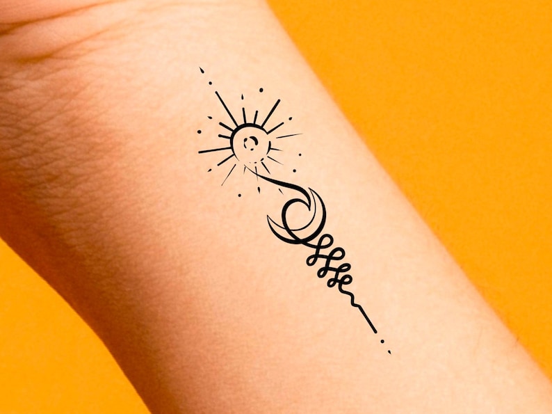 May include: A black and white tattoo design of a sun, moon, and a spiral on a person's wrist.