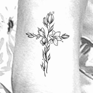 May include: A black and white line drawing of a cross with flowers growing from the centre.