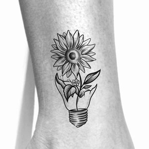 Puede incluir: Dise&ntilde;o de tatuaje en blanco y negro de un girasol que crece fuera de una bombilla rota.