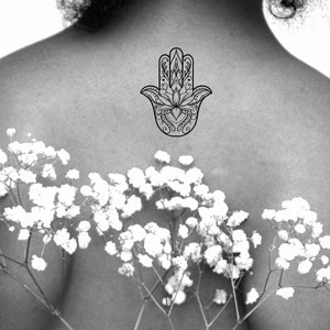 May include: A black and white hamsa hand tattoo design with intricate details.