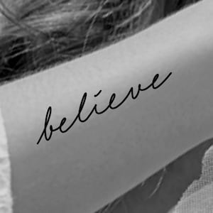 May include: A black and white image of a temporary tattoo that says "believe" in a cursive font.