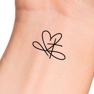 May include: A simple black line drawing of a heart with a cross inside, on a light skin tone background.