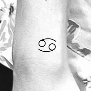 May include: A black line drawing of the Cancer zodiac symbol on a person's arm.