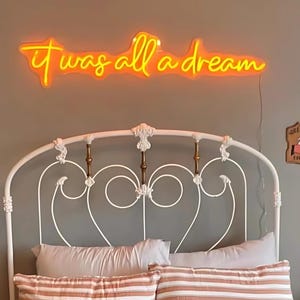Puede incluir: Una estructura de cama de metal blanco con una cabecera con un dise&ntilde;o decorativo de volutas. Encima de la cama hay un letrero de ne&oacute;n que dice "it was all a dream".