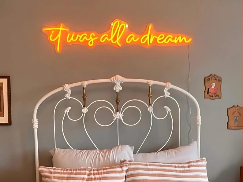 Puede incluir: Una estructura de cama de metal blanco con una cabecera con un dise&ntilde;o decorativo de volutas. Encima de la cama hay un letrero de ne&oacute;n que dice "it was all a dream".
