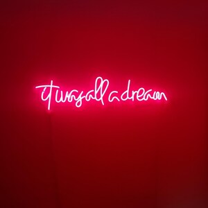 Puede incluir: Un letrero de ne&oacute;n en una pared roja que dice "it was all a dream".