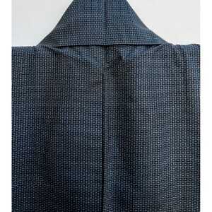 May include: A black kimono with a blue and white geometric pattern. The kimono is folded and hung on a hanger.