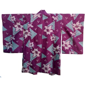 May include: A purple kimono with a floral pattern. The kimono features white flowers and light blue triangles. The garment is made of a soft fabric and has wide sleeves.
