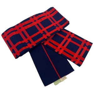 Puede incluir: Bufanda estampada en azul marino y rojo. La bufanda presenta un patrón de cuadrícula en rojo sobre un fondo azul marino. También se ve una sección azul marino liso con una raya roja. Se adjunta una pequeña etiqueta.